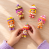 Vista desde arriba de unas manos infantiles sujetando una muñeca Pinypon Cupcakes junto a otras cuatro figuras sobre una mesa.