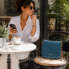 Mujer disfrutando de un café con bolso Desigual Varsovia azul pequeño bandolera modelo 18WAXPXU apoyado sobre una silla