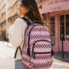 Mujer joven caminando por ciudad con mochila Vans rosa checkerboard grande estilo urbano. Imagen lifestyle optimizada para Google Imágenes, Pinterest y ecommerce de mochilas mujer.