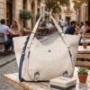 Bolso grande Desigual Minuet Rotterdam beige apoyado en una mesa de madera de una cafetería soleada, mostrando su diseño bordado y detalles premium. Una imagen que transmite elegancia y estilo diario, ideal para regalo. Disponible en amathingshop.com.
