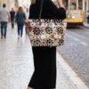 Estilo Calle con Bolso Grande Desigual Multicolor Artístico Mujer elegante caminando por una calle adoquinada de una ciudad europea, vistiendo un vestido de punto negro y zapatillas blancas, sosteniendo el bolso grande Desigual multicolor con diseño de mosaico geométrico y acabado efecto piel de reptil. Foto de estilo de vida que muestra el tamaño real y la versatilidad del bolso. Disponible en amathingshop.com.