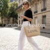 Bolso Desigual Grande Alola Holbox Beige - Edición LOVE Mujer elegante caminando por la calle usando el bolso grande Desigual Alola Holbox beige con el mensaje LOVE, ideal para trabajo o universidad. Edición limitada disponible en amathingshop.com.