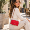 Mujer sentada en una terraza con bolso monedero Desigual Hela Carmen rojo, diseño floral en relieve, efecto reptil y correa marrón.