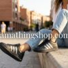 Primer plano lateral de zapatillas Adidas Grand Court negras con tres bandas plateadas y suela de goma negra, puestas por una chica sentada, de amathingshop.com.