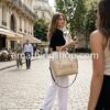 Estilo Calle con Bolso Grande Desigual LOVE Beige Mujer elegante caminando por una calle adoquinada de una ciudad europea vistiendo pantalones de lino blancos y sosteniendo el bolso grande Desigual Alola Holbox beige con el mensaje LOVE. Foto de estilo calle que muestra el tamaño real y la versatilidad del bolso. Disponible en amathingshop.com.