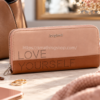 Cartera grande Desigual Rhapsody LOVE YOURSELF rosa y marrón, con cremallera, junto a bolso y accesorios de mujer.