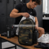 Mochila Vans camuflaje 27L para gimnasio, trabajo y uso diario Mochila Vans camuflaje de 27 litros utilizada en vestuario de gimnasio con ropa deportiva, botella y accesorios para combinar entrenamiento y trabajo.