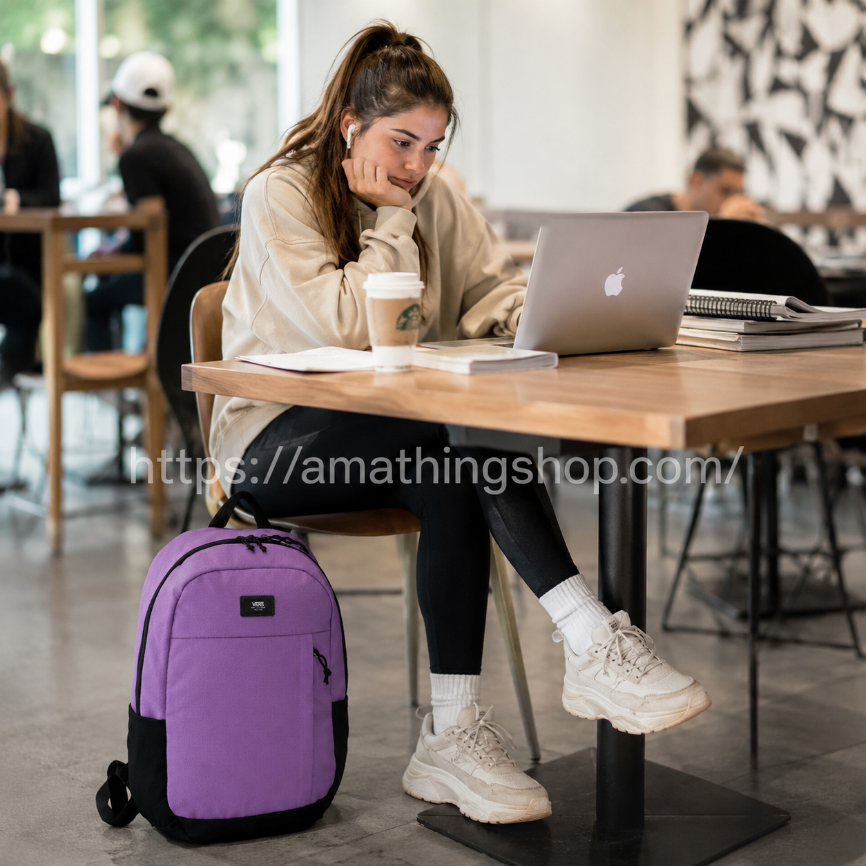 mochila-vans-lila-universidad-cafe-lifestyle-premium Mochila Vans lila premium junto a estudiante en cafetería moderna con portátil