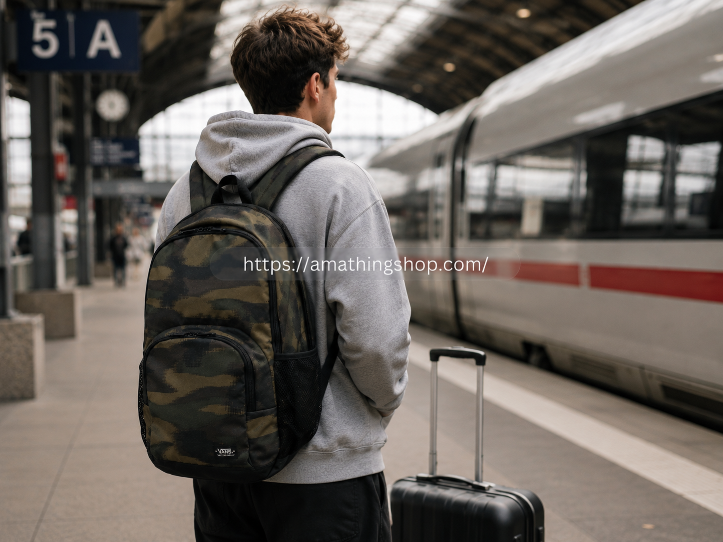 Mochila Vans camuflaje 27L para viajes de fin de semana y escapadas cortas Joven esperando en una estación de tren con mochila Vans camuflaje de 27 litros y maleta de cabina para una escapada de fin de semana.