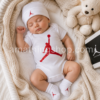 Bebé recién nacido durmiendo con conjunto Nike Air Jordan de 3 piezas blanco y rojo compuesto por body, gorro y patucos modelo MJ0041-001 en un capazo de punto