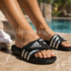 Primer plano de unas chanclas Adidas Adissage negras con plantilla de masaje usadas por una mujer junto a una piscina en verano.