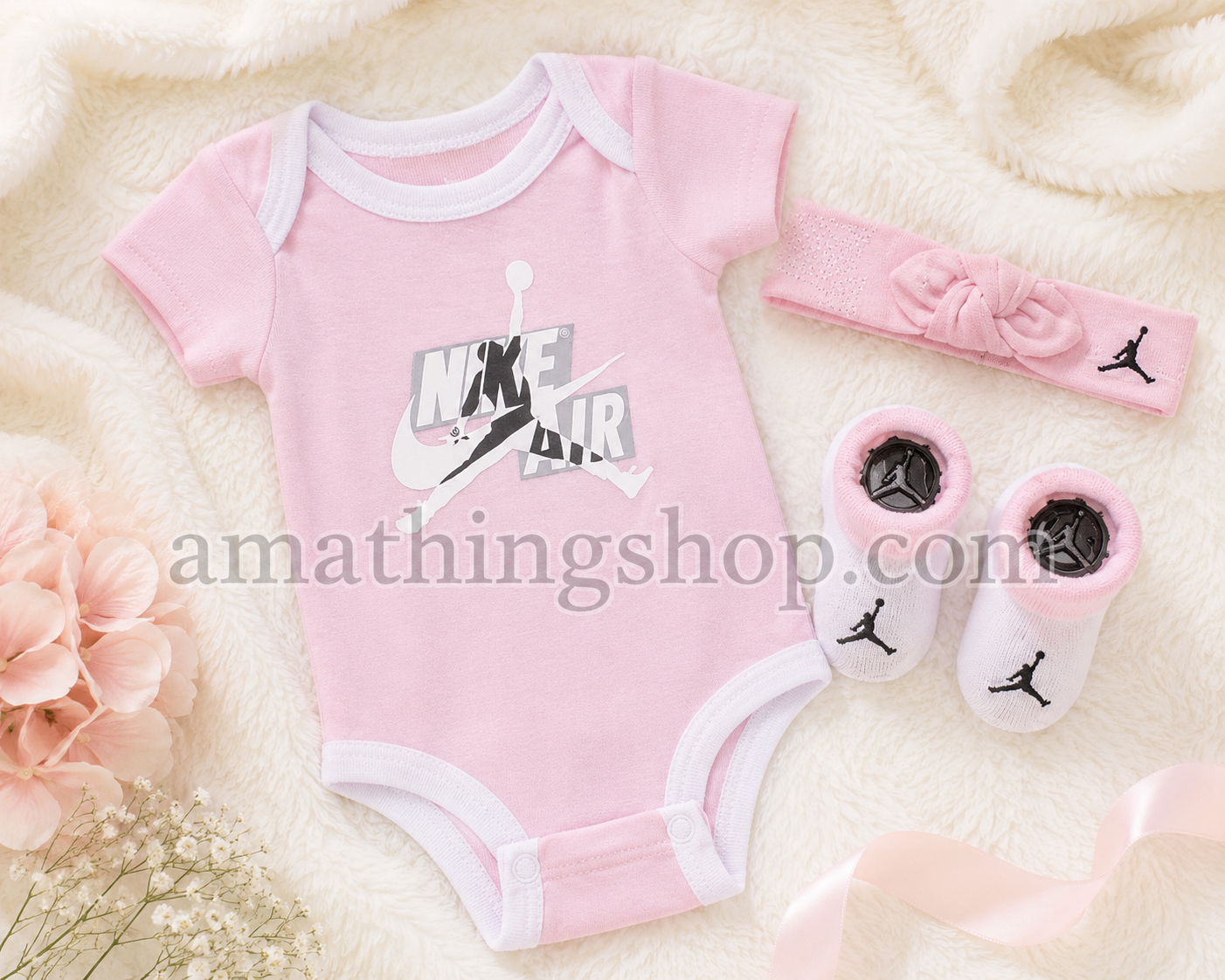 Conjunto Jordan Jumpman para bebé niña compuesto por body rosa, diadema y patucos sobre manta suave en tonos pastel.