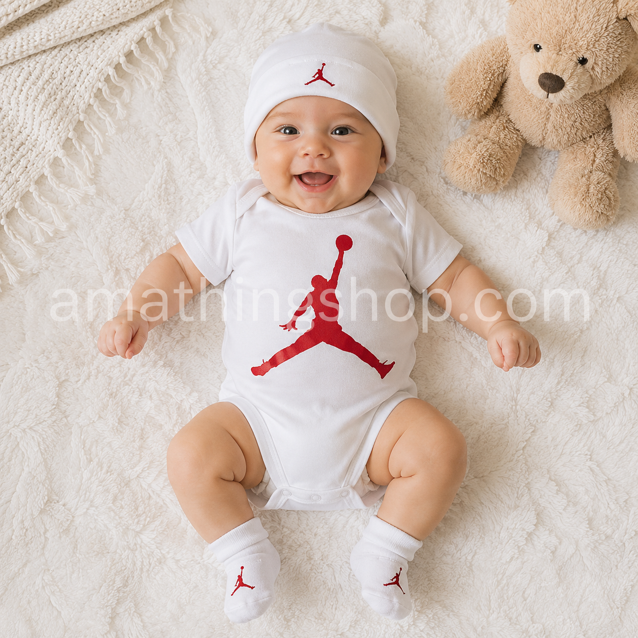 Bebé sonriendo con conjunto Nike Air Jordan de 3 piezas blanco y rojo compuesto por body, gorro y patucos modelo MJ0041-001 para 0-6 meses