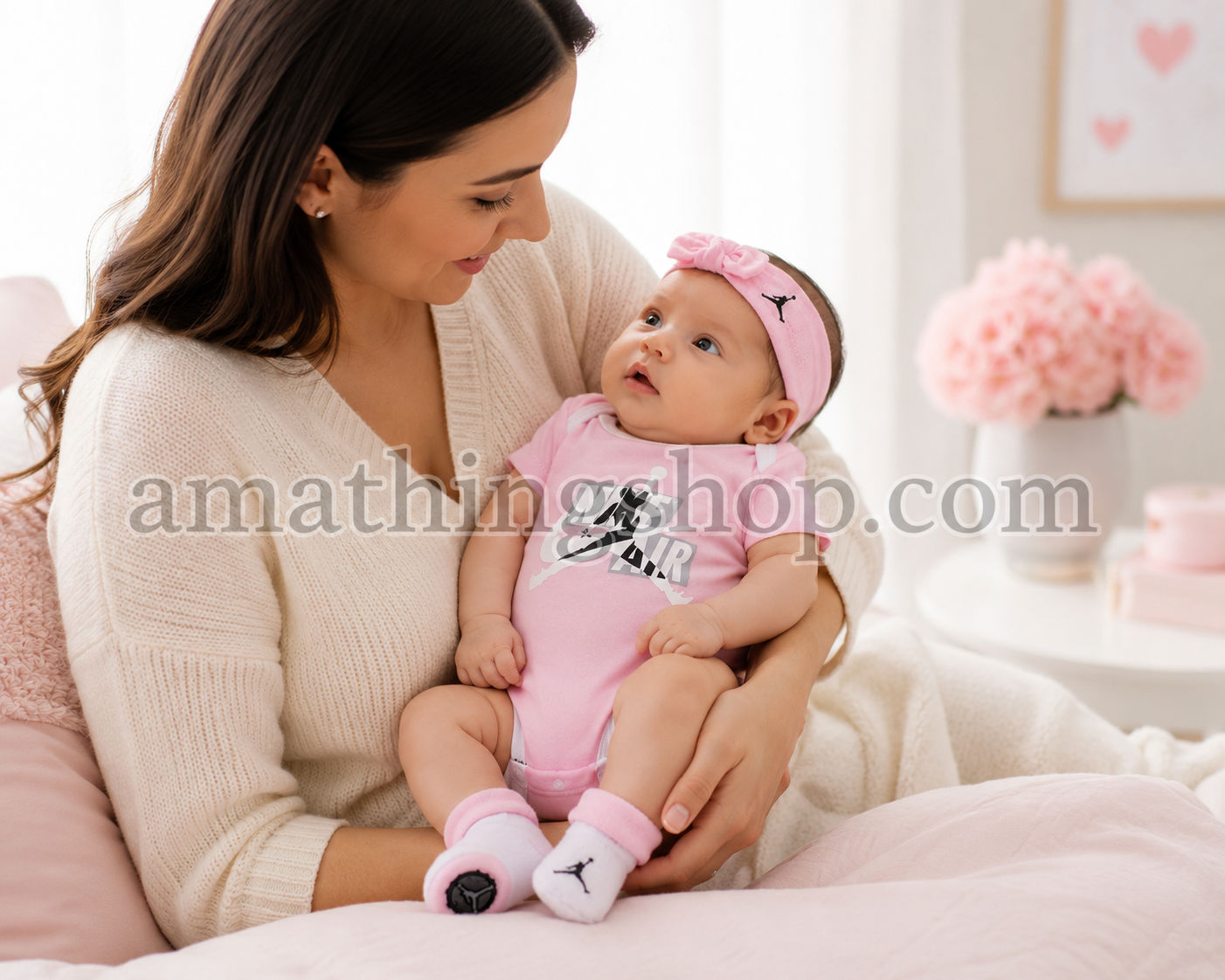 Mamá abrazando a su bebé recién nacida vestida con conjunto Jordan rosa de body, diadema y patucos en una habitación luminosa.