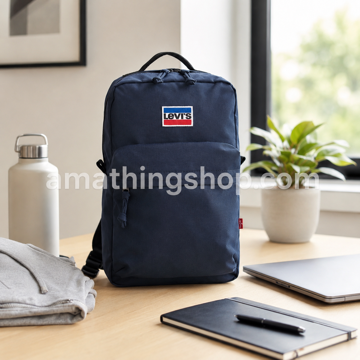 Mochila Levi’s Mini L Pack azul marino 13L sobre escritorio con portátil, libreta, botella y sudadera, ideal para trabajo, universidad, gimnasio, paseos diarios y escapadas ligeras.