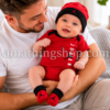 Bebé sonriente con conjunto Jordan rojo compuesto por body, gorro y patucos sobre ambiente cálido familiar.