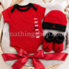 Canastilla para recién nacido con conjunto Jordan rojo compuesto por body, gorro y patucos sobre manta suave.
