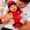 Padre sosteniendo a su bebé recién nacido con conjunto Jordan rojo de body, gorro y patucos.