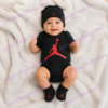 Bebé con conjunto Nike Jordan de 3 piezas formado por body negro, gorro y patucos con logotipo Jumpman rojo modelo MJ0041-023 0-6 meses