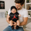 Padre sujetando a un bebé vestido con el conjunto oficial Nike Jordan de body negro, gorro y patucos con logotipo Jumpman rojo