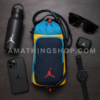 Bandolera Nike Jordan portabotellas azul y amarillo con botella, móvil, reloj y gafas en composición flat lay lifestyle.