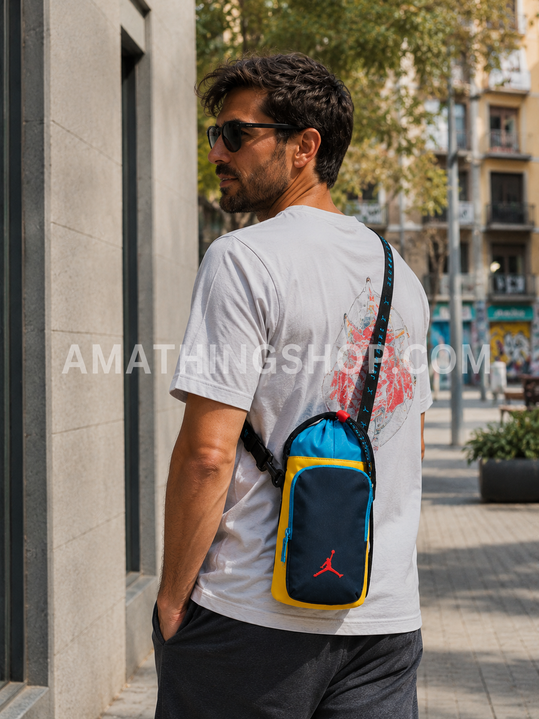 Hombre usando bandolera Nike Jordan portabotellas azul y amarillo mientras pasea por ciudad en ambiente urbano lifestyle.