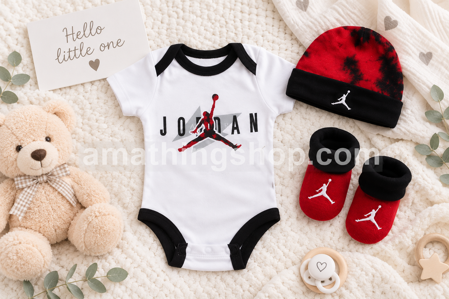 Body Nike Air Jordan para bebé con gorro rojo y negro y patucos a juego sobre fondo de manta blanca con peluche y chupete modelo NJ0446-001