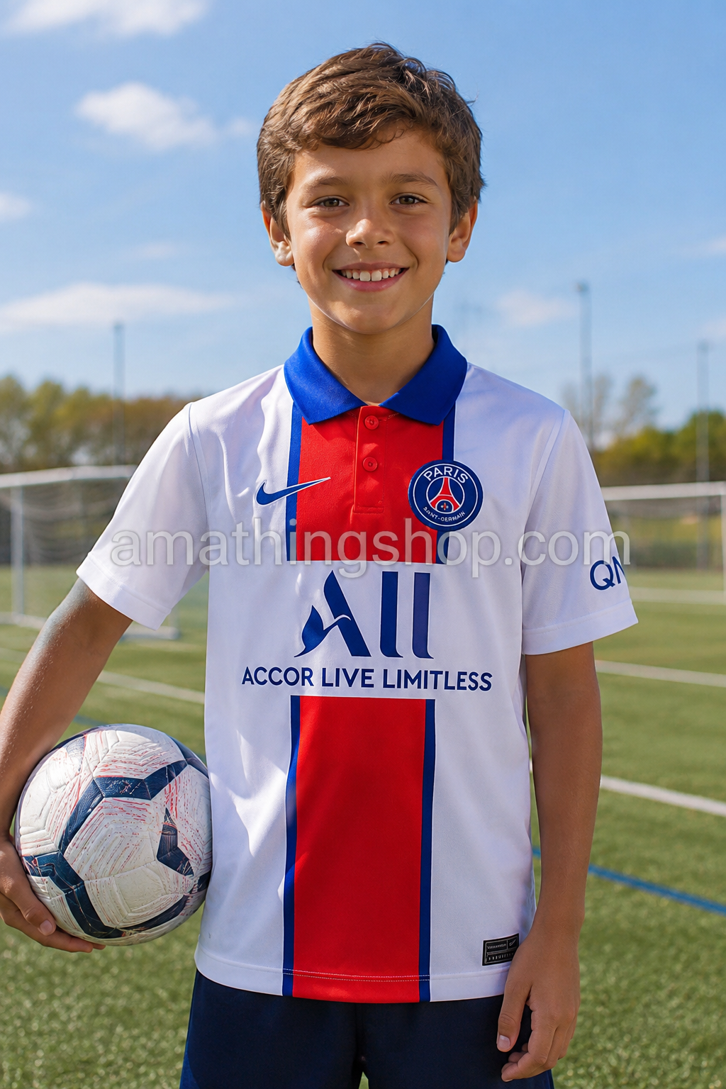 Niño sonriendo en campo de fútbol con camiseta oficial Nike PSG 2020/21 blanca para niño, diseño visitante del Paris Saint-Germain con detalles rojos y azules. Imagen lifestyle deportiva orientada a fútbol infantil y regalo original para fans del PSG.