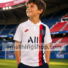 Niño con camiseta PSG Nike blanca oficial en estadio de fútbol con diseño deportivo infantil transpirable.