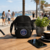 Bolso bandolera Jordan Paris Saint-Germain negro sobre mesa de cafetería frente al mar con café y móvil, accesorio urbano oficial PSG para hombre y mujer