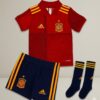 Conjunto de fútbol infantil de la selección de España compuesto por camiseta roja, pantalón azul marino y medias, presentado en estilo catálogo premium sobre fondo neutro.