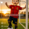 Bebé celebrando con equipación roja de España y balón de fútbol junto a portería al atardecer estilo lifestyle premium