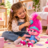 Niña jugando con la muñeca interactiva Poppy de Trolls World Tour, con melena rosa, vestido azul y patines.