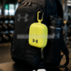Estuche deportivo Under Armour amarillo colgado en mochila negra de gimnasio con auriculares y botella estilo lifestyle premium
