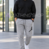 Hombre rubio de unos 40 años con pantalón Jordan Jumpman gris XL, logo negro, sudadera negra y zapatillas blancas en un entorno urbano. Copiar ALT