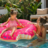 Madre e hija jugando en una piscina con un flotador donut fresa rosa de aproximadamente 110 cm durante un día de verano en un jardín con piscina privada.