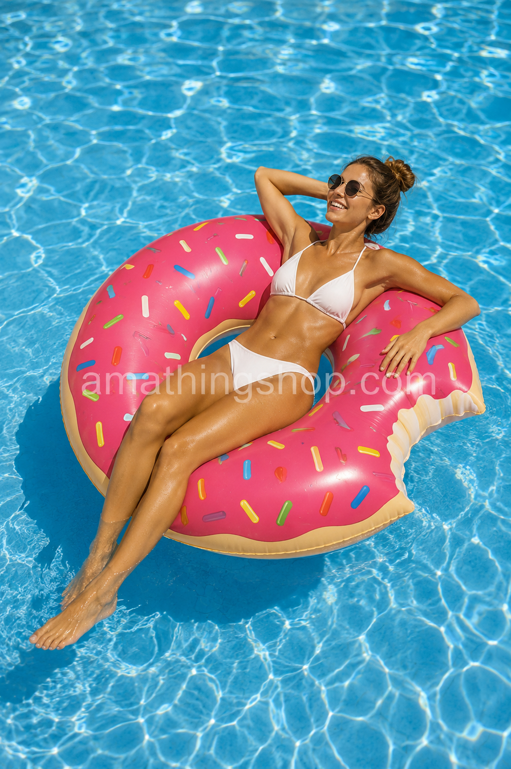 Mujer relajándose sobre flotador donut fresa rosa de 110 cm aproximadamente en una piscina azul durante un día de verano, con diseño divertido tipo donut mordido y web Amathingshop.com integrada.