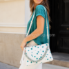 Mujer llevando bolso Desigual New Splatter Dortmund Maxi blanco 24SAXP10-1000 con estampado de gotas verde turquesa, cadena metálica y correa ajustable.