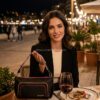 Bolso Desigual Prime Urus Maxi Negro - Estilo Noche y Eventos Mujer elegante durante una cena nocturna llevando el bolso Desigual Prime Urus Maxi negro. Se aprecia el acabado premium efecto piel, los detalles trenzados y su tamaño mediano ideal para eventos. Ambiente de lujo con luces cálidas de fondo. Disponible en amathingshop.com.