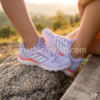 Primer plano detallado de zapatillas Adidas Terrex lila con bandas blancas y detalles naranjas, calzado de montaña para mujer en ambiente exterior