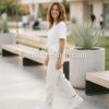 look-lifestyle-mujer-converse-blancas-bordadas Mujer joven con outfit casual beige y zapatillas Converse blancas bordadas caminando por un parque moderno, imagen de amathingshop.com