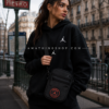 Mujer usando bandolera Jordan PSG negra estilo streetwear urbano en ciudad europea inspirada en París.