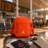 Bolso Jordan Airborne naranja lifestyle viaje aeropuerto Bolso Jordan Airborne naranja sobre maleta de cabina en aeropuerto moderno con accesorios de viaje. Imagen lifestyle optimizada para Google Imágenes, Pinterest y ecommerce streetwear.
