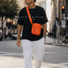 Bolso Jordan Airborne naranja hombre lifestyle urbano ciudad Hombre joven caminando por ciudad moderna usando bolso Jordan Airborne naranja estilo bandolera streetwear. Imagen lifestyle optimizada para Google Imágenes, Pinterest y ecommerce urbano.