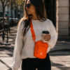 Bolso Jordan Airborne naranja mujer lifestyle urbano moderno Mujer joven caminando por ciudad moderna con bolso Jordan Airborne naranja estilo bandolera y café en mano. Imagen lifestyle optimizada para Google Imágenes, Pinterest y ecommerce urbano.