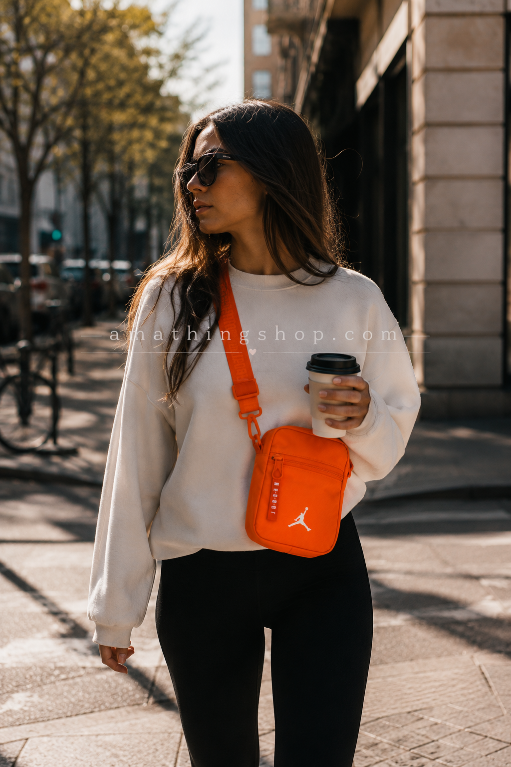 Bolso Jordan Airborne naranja mujer lifestyle urbano moderno Mujer joven caminando por ciudad moderna con bolso Jordan Airborne naranja estilo bandolera y café en mano. Imagen lifestyle optimizada para Google Imágenes, Pinterest y ecommerce urbano.