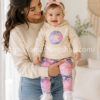 Madre sujetando bebé niña con conjunto Converse beige y leggings rosa estampado premium