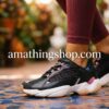 Primer plano de las zapatillas Reebok Royal Pervader negras con detalles rosa y suela blanca, puestas con leggings granates en un entorno urbano, de amathingshop.com.