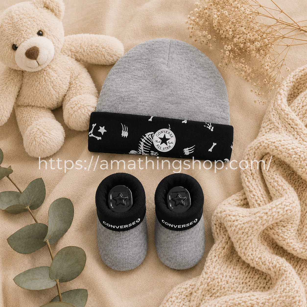 Conjunto Converse bebé gris y negro con gorro y calcetines sobre manta beige premium