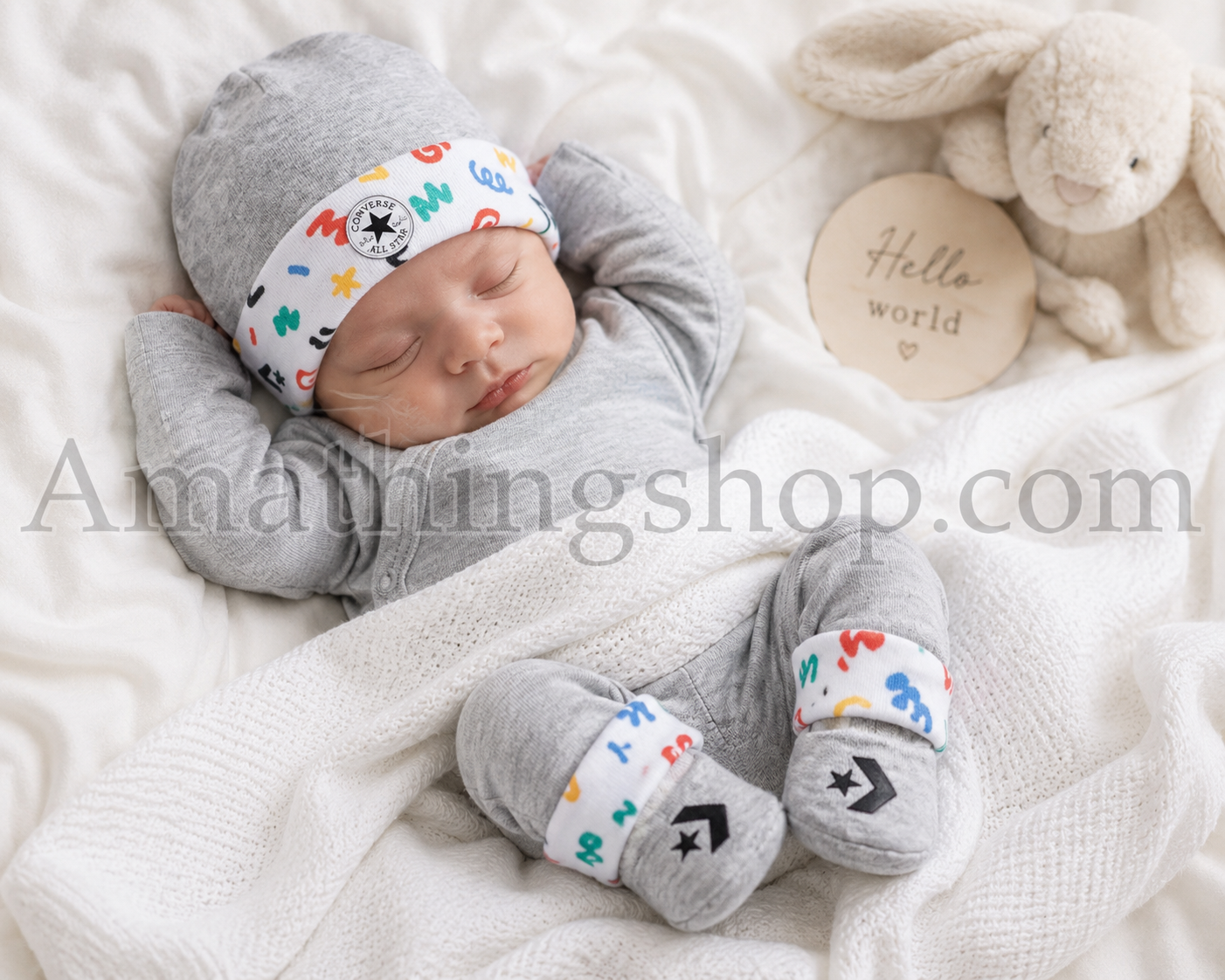 Bebé recién nacido descansando con conjunto Converse de gorro y patucos gris multicolor para 0 a 6 meses, ideal como regalo de nacimiento.